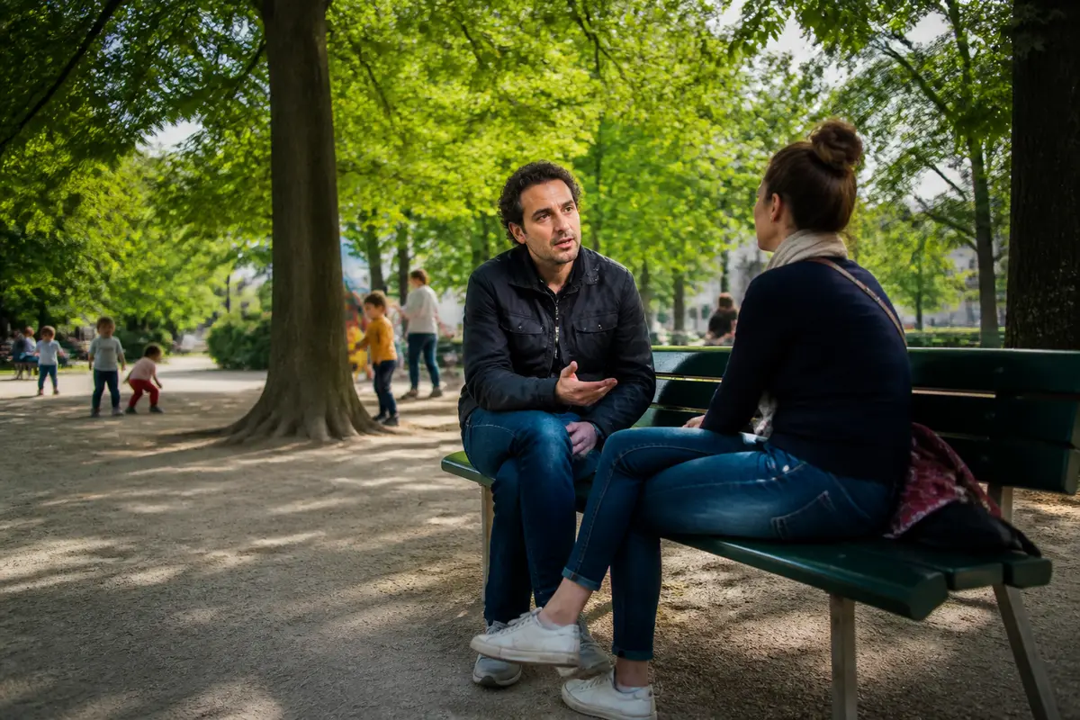 Deux personnes discutent sur un banc dans un parc, illustrant le coaching de vie parisien