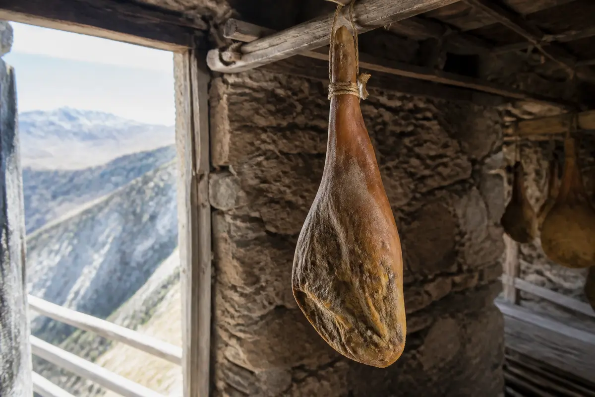 Jambon type Serano suspendu dans une cave en pierre avec vue montagneuse